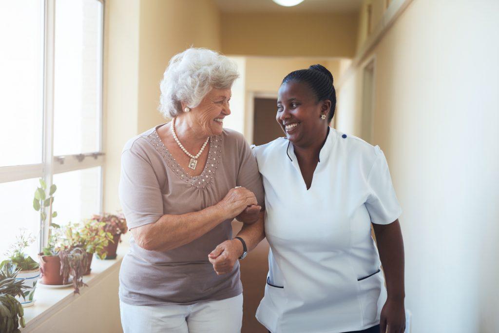 Older woman walking with nurse in residential senior care building