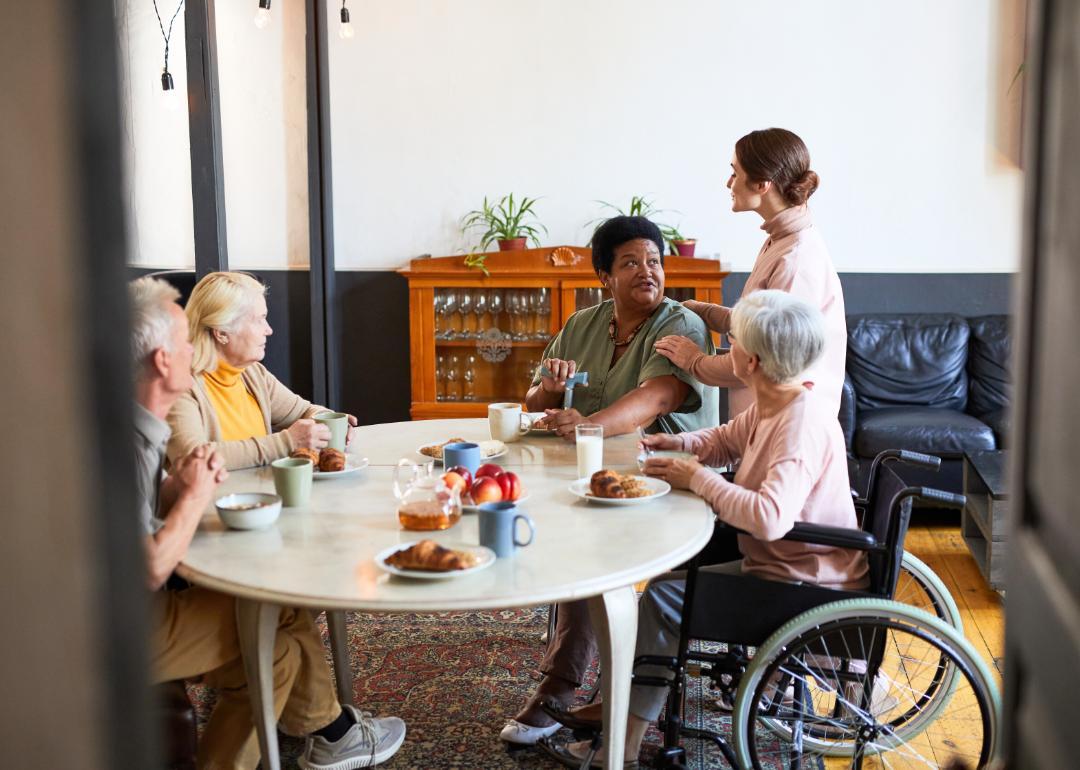 Multicultural group of nursing home residents having breakfast with aide